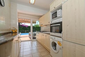 A kitchen with a washing machine, oven, microwave, and a view to an outdoor area. - Casa Siboc – Mediterranean villa with a pool (Benissa)