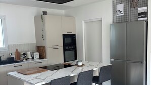 Et moderne køkken med en central ø, barstole, indbygget ovn og et rustfrit stålkøleskab.