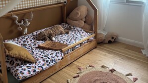 Et hyggeligt værelse med væg i skakmønster, en seng med sengetæppe i et mønster, en hængende lysarmatur og et stort vindue med persienner.