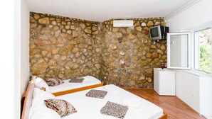 Ein Schlafzimmer mit zwei Betten, Steinwänden, einem Fernseher und einem kleinen Kühlschrank.