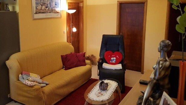 Una sala de estar con un sofá, un sillón con un cojín con forma de corazón, una mesita con un adorno y una estatua.