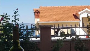 Un edificio con techo de tejas rojas y fachada blanca, una cerca de metal y una botella en primer plano.