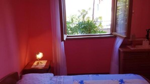 Un dormitorio con cama, mesita de noche, ventana con cortinas y vista a la vegetación.