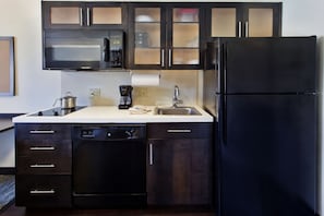 Una cocina moderna con armarios oscuros, microondas, cafetera y lavavajillas.