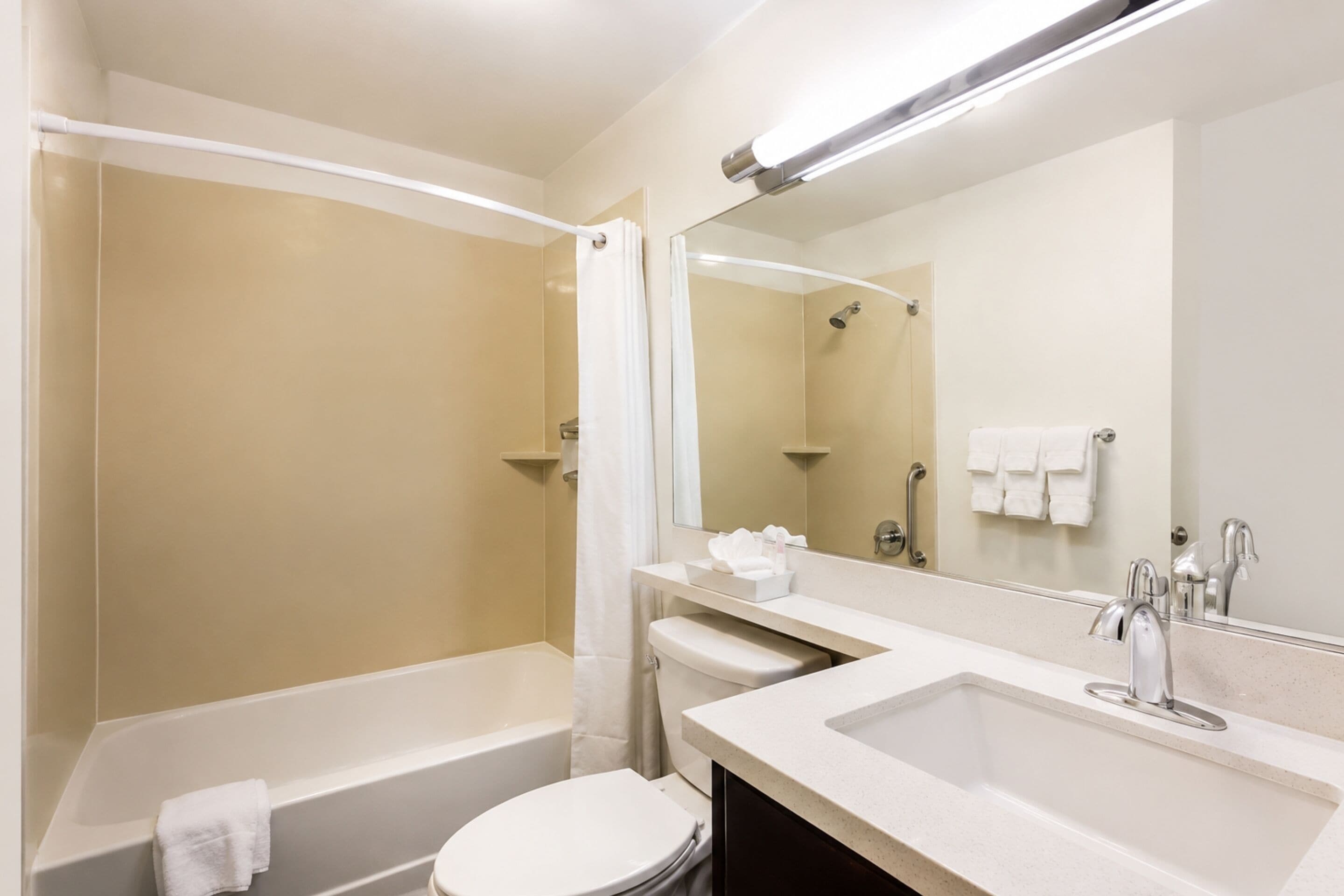 A modern bathroom with a bathtub, toilet, and sink, featuring a large mirror and a shower curtain.