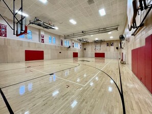Un campo da basket con tabellone segnapunti, finestre e protezioni rosse alle pareti.