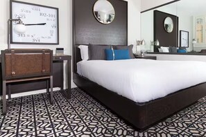 Camera d'albergo moderna con un letto grande, una scrivania con una lampada, uno specchio e una sveglia a muro che mostra equazioni matematiche.