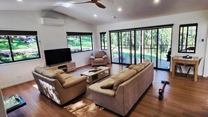 Uma sala de estar ampla, com sofá, televisão e um espaço de jantar com mesa e cadeiras.
