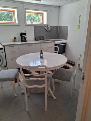 Uma cozinha compacta com uma mesa de jantar redonda, cadeiras brancas, máquina de café e micro-ondas.
