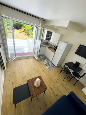 A compact living space with a kitchenette, a dining area, and a sliding glass door leading to an outdoor area. - Charming Parisian Apartment with Garden View (Paris)