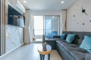 Ein modernes Wohnzimmer mit einer Couch, einem Flachbildfernseher, einer Marmorwand und einem großen Fenster.