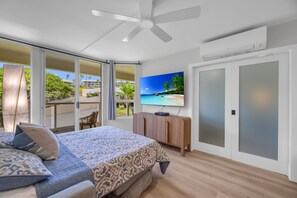 A bedroom with a bed, a TV, a ceiling fan, and a sliding glass door to a balcony. - 2 2 New Designer Beachside Resort Vistas (Kihei)