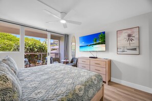 A bedroom with a bed, a TV, a desk, and a balcony with outdoor furniture. - 2 2 New Designer Beachside Resort Vistas (Kihei)