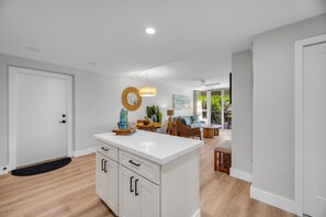 Una cocina moderna con armarios blancos, una isla central y un comedor con mobiliario de mimbre.