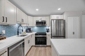 A modern kitchen with white cabinets, stainless steel appliances, and a blue-tiled backsplash. - 2 2 New Designer Beachside Resort Vistas (Kihei)