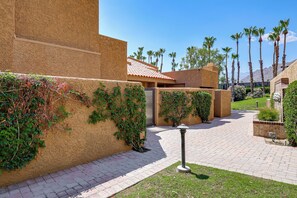 A courtyard with a brick pathway, palm trees, and a building with a red-tiled roof. - Private Hot Tub + Rooftop Patio: Palm Desert Oasis (Palm Desert)