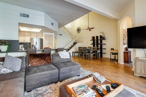 Ein geräumiger Wohnbereich mit einem grauen Ecksofa, einem Holztisch und einer Küche im Hintergrund.