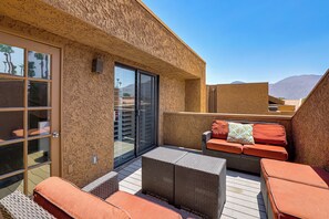 An outdoor patio with wicker furniture, a glass door, and a view of mountains. - Private Hot Tub + Rooftop Patio: Palm Desert Oasis (Palm Desert)