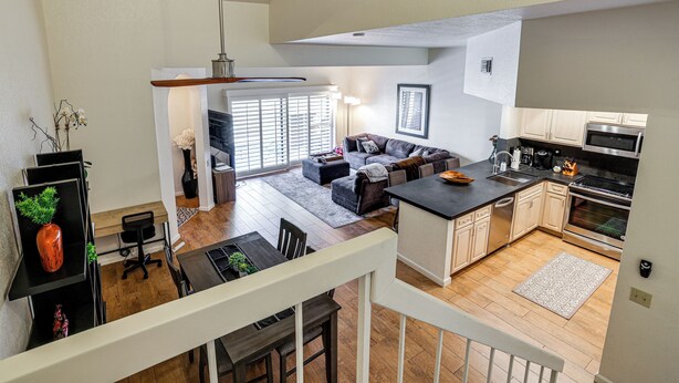 Et moderne køkken med en central ø, et spiseområde med bord og stole, en stue med sofa og sofabord, og en trappe til en etage ovenpå.