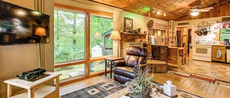Interior acogedor de una cabaña con chimenea, sillón de cuero, muebles de madera y un ventanal con vistas al exterior.