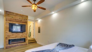 Une chambre avec un mur en bois, un ventilateur de plafond, une télévision, une cheminée et un lit avec une couverture.