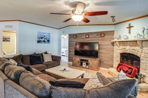 Ein Wohnzimmer mit Ecksofa, Flachbildfernseher, Kamin und Deckenventilator.