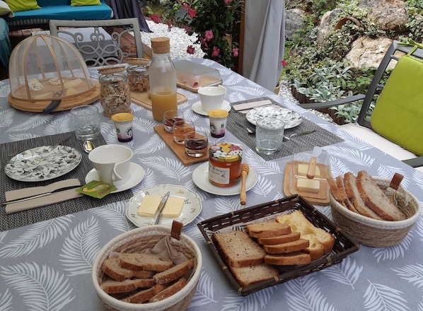 A table set with various food items, including bread, cheese, and condiments, in an outdoor dining area with a view of plants and rocks.