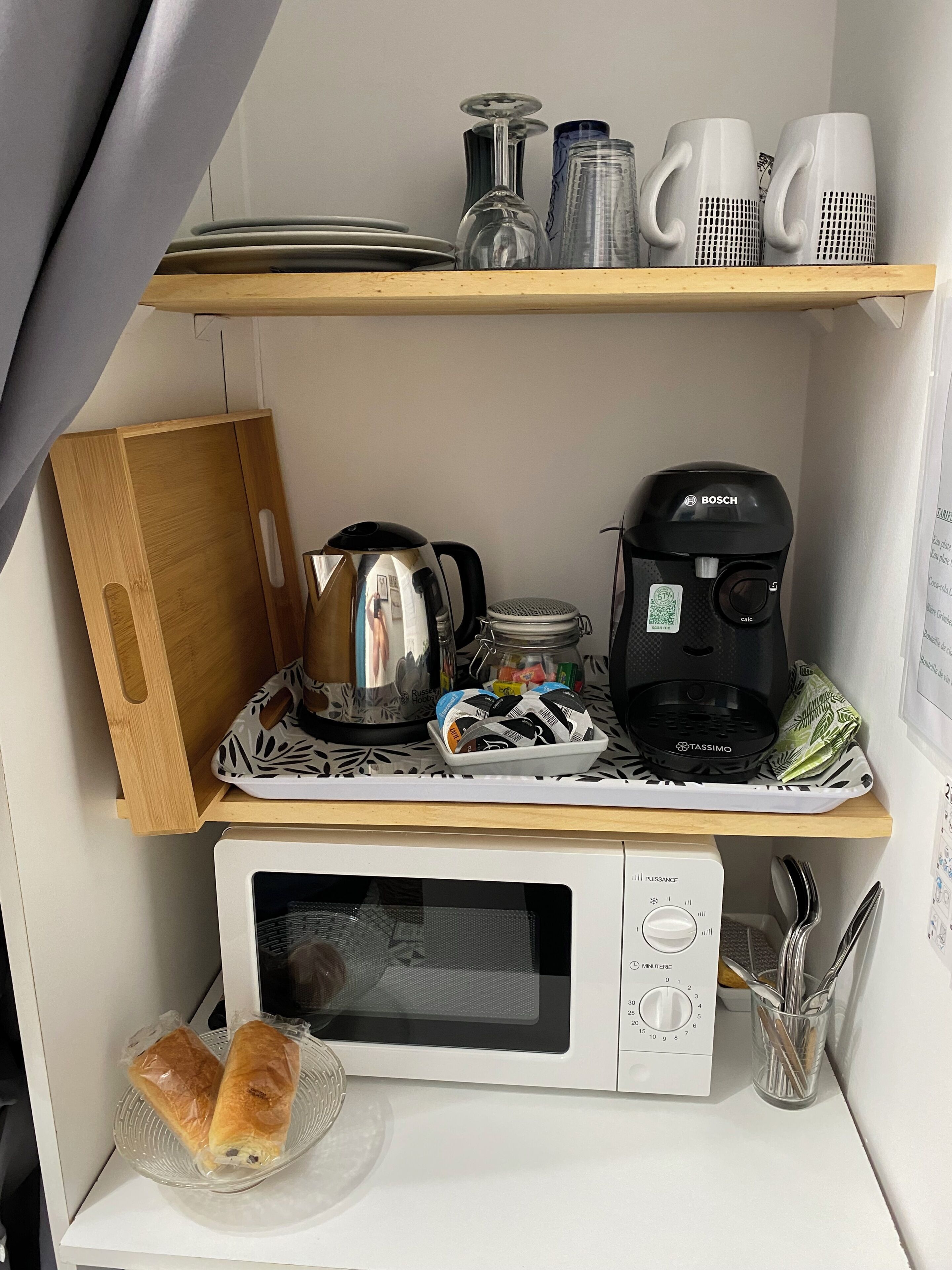 A kitchenette with a microwave, coffee maker, kettle, and various kitchen utensils.