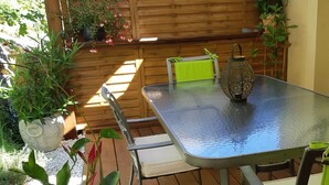 A wooden deck with a metal table and chairs, surrounded by potted plants and a wooden fence. - Le Val du Loup Bed and Breakfast: Continental breakfast available upon request (Sanilhac)
