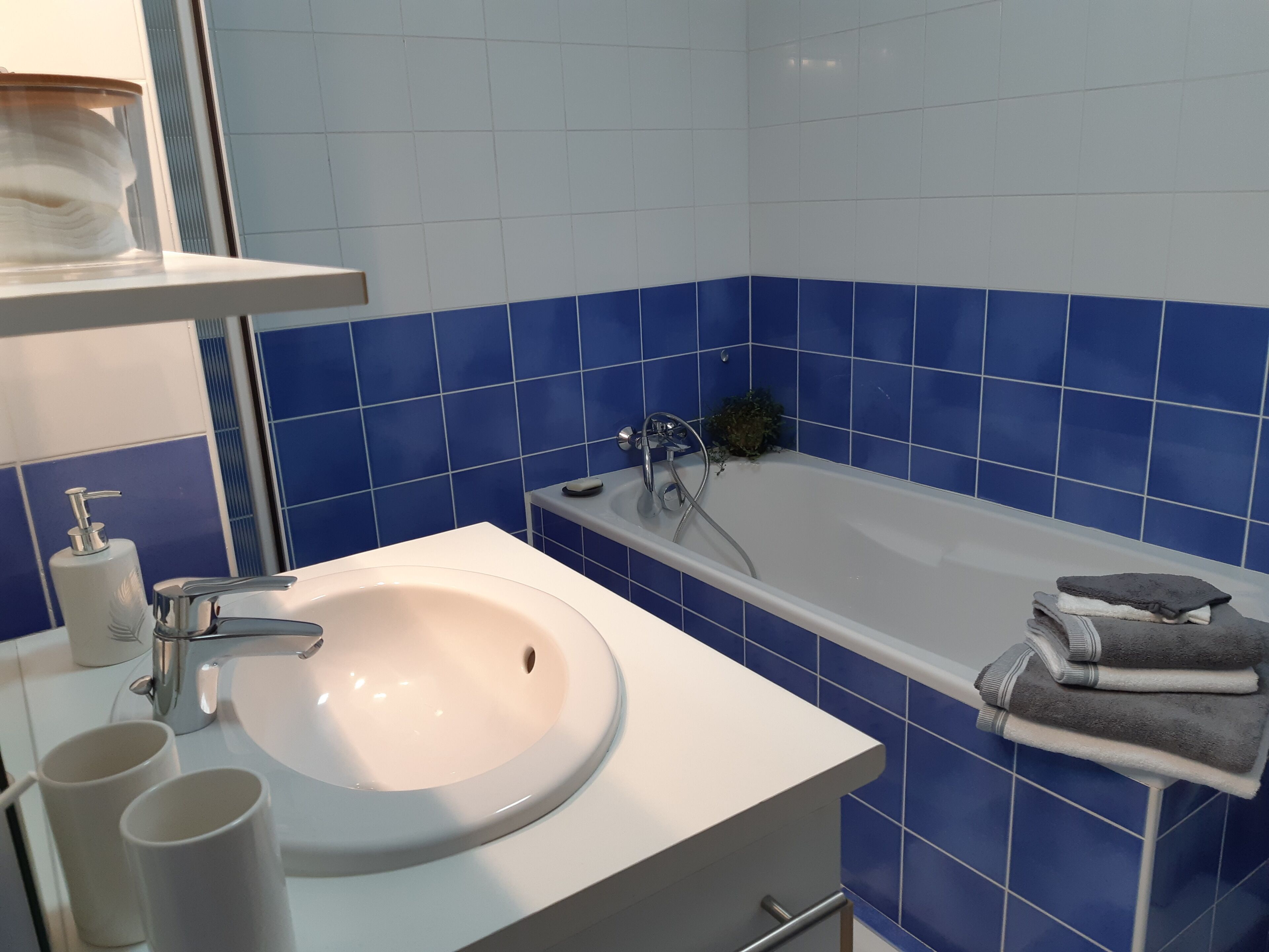 Une salle de bain avec un lavabo blanc, des carreaux bleus, une baignoire et un porte-serviettes.