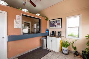 Un espace d’accueil comprenant un comptoir, une poubelle, un coin café et un tableau encadré au mur.