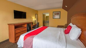Ein Hotelzimmer mit Bett, Schreibtisch, Stuhl, Fernseher und Spiegel.