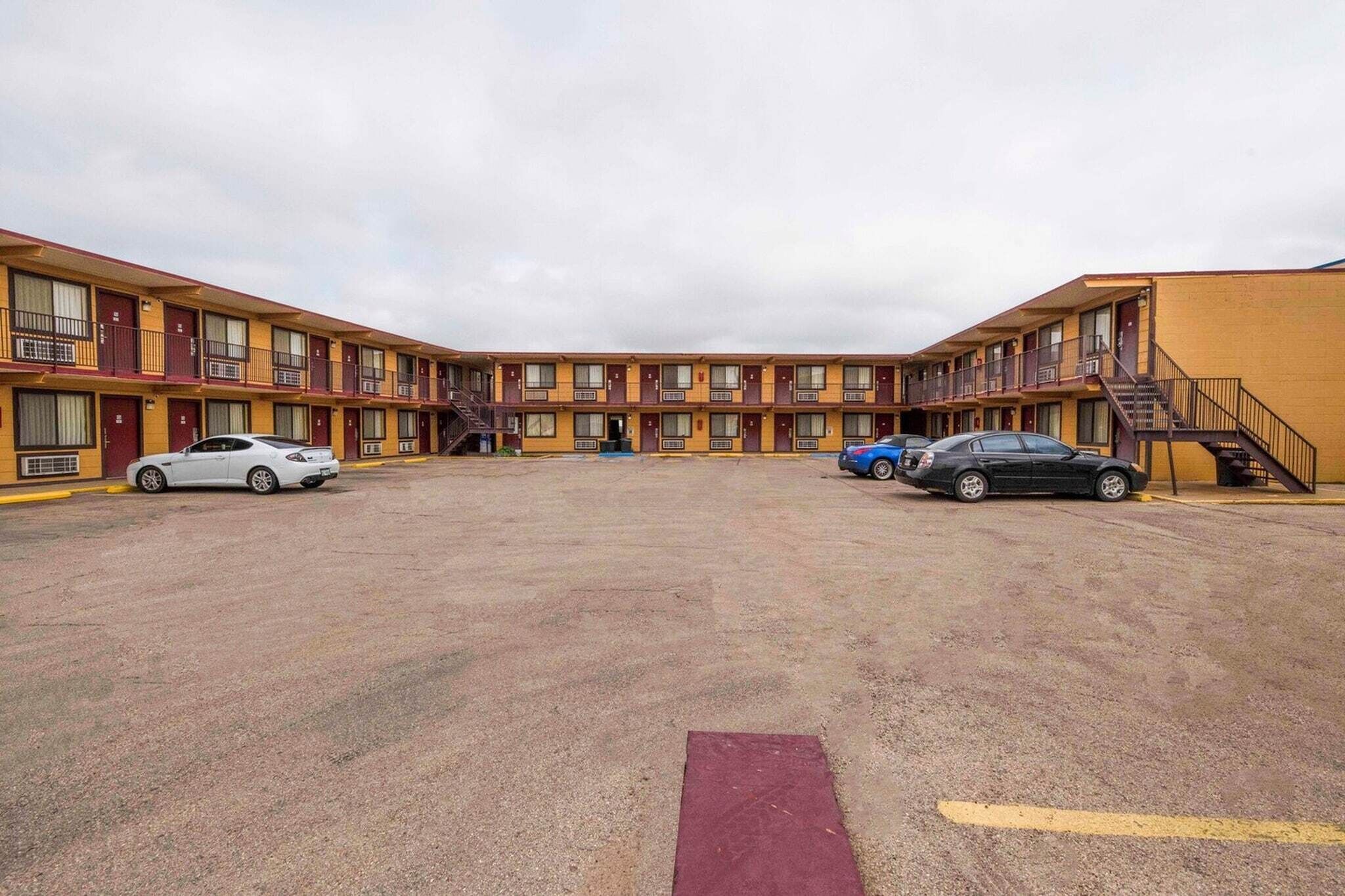 A motel with a central courtyard, multiple floors, and a parking area with cars.