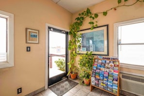Un hall d’hôtel avec une porte, un tableau encadré, une plante en pot, un panneau d’affichage avec des brochures de voyage et une fenêtre avec des stores.