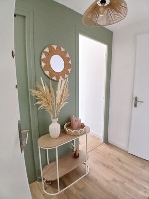 Ein Zimmer mit grüner Wand, einem runden Spiegel, einem kleinen weißen Tisch mit Kerzen und einem gewebten Korb.