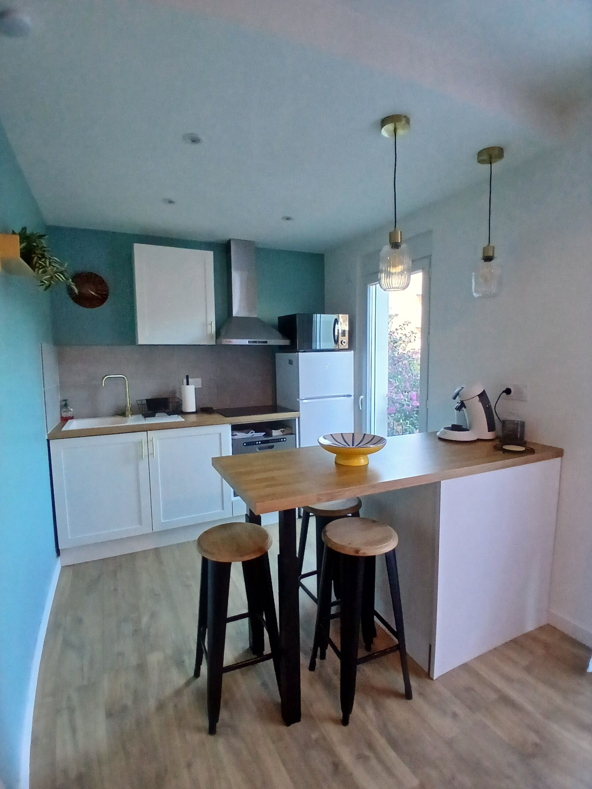 Une cuisine moderne avec des meubles blancs, un îlot central en bois doté de tabourets et un éclairage suspendu.