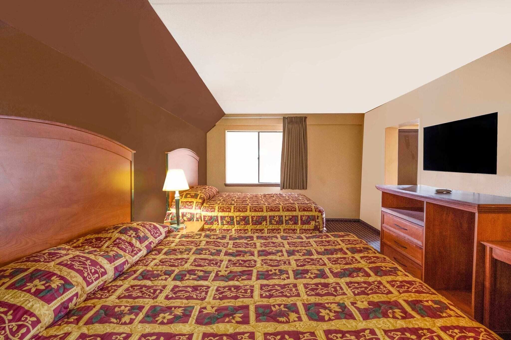 A hotel room with a large bed, a desk, a television, and a window with curtains.
