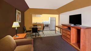 Une chambre d’hôtel compacte comprenant un coin cuisine, un téléviseur posé sur un meuble en bois, un coin repas avec des chaises et un canapé.