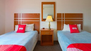 A hotel room with two beds, each with a red pillow and a wooden headboard. There is a nightstand with a lamp between the beds. - 2 Full Beds | Non-Smoking (Redwood Falls)