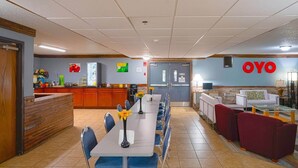 Un hall d’hôtel comprenant un comptoir d’accueil, une longue table à manger avec des chaises, un canapé et un mur sur lequel est inscrit le mot « OYO ».
