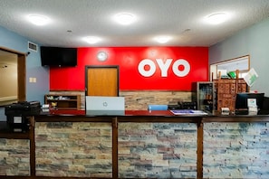 A reception desk with a red wall, a clock, and a sign that reads 'OYO'.