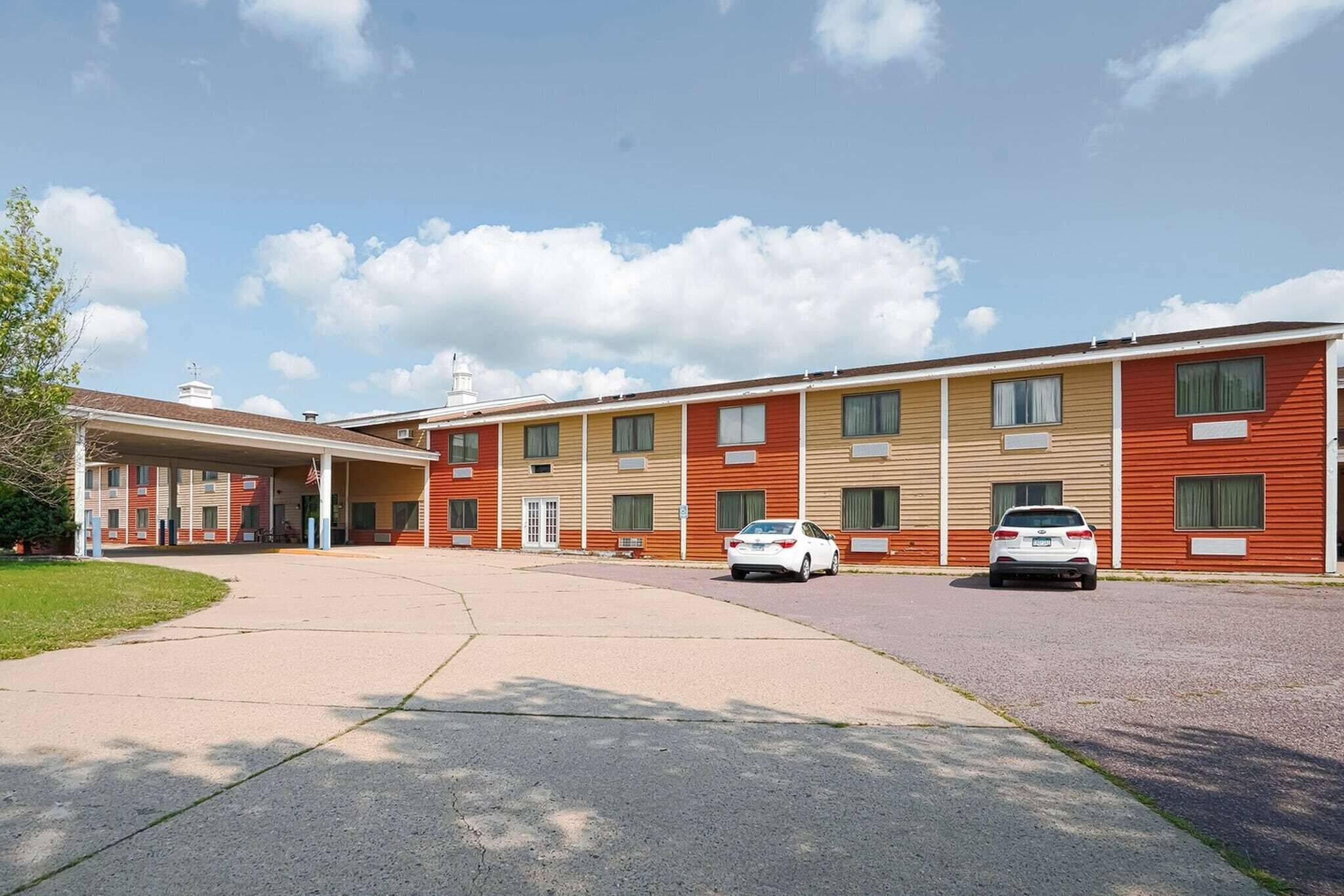 A motel with a covered parking area, multiple-story buildings, and cars parked in front.