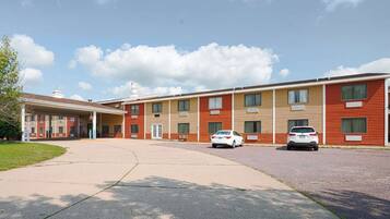A motel with a covered parking area, multiple-story buildings, and cars parked in front.