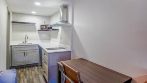 A compact kitchen with a microwave, sink, and stove, a small table, and a chair.