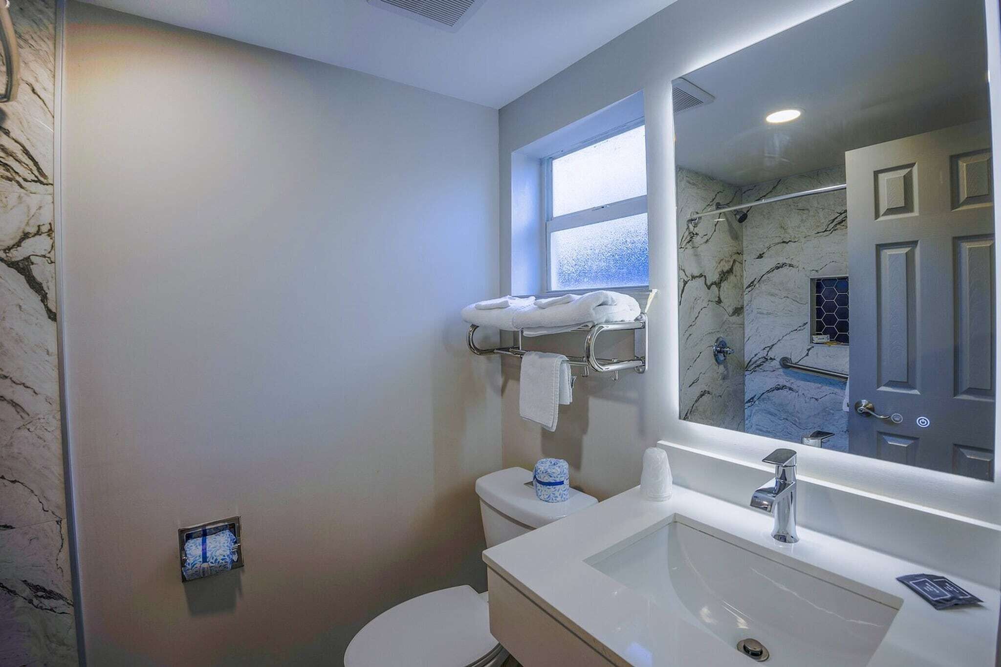 Een badkamer met een witte wasbak, een spiegel, een handdoekrek en een toilet.