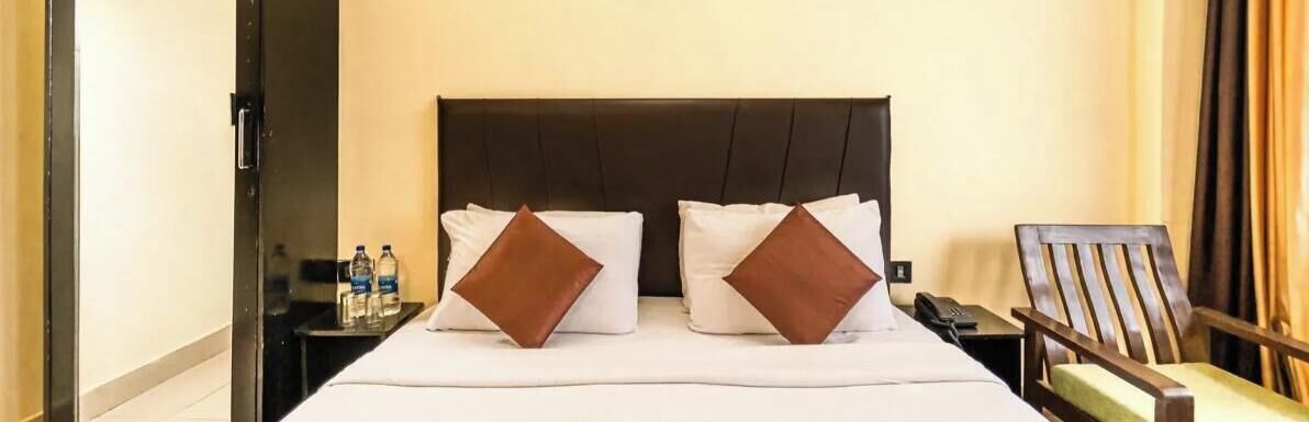 Une chambre d’hôtel avec un lit, des oreillers, une table de chevet, une chaise et une porte.