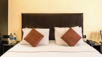 Une chambre d’hôtel avec un lit, des oreillers, une table de chevet, une chaise et une porte.