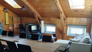 A wooden interior with a dining table, chairs, a sofa, a TV, and a window. - La Canissa Carrada Vacation Rental for 4 to 6 People (Chaspuzac)