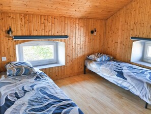 Une cabane avec deux lits, des murs en bois, une fenêtre et un luminaire.