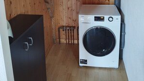 A compact laundry room with a white washing machine, a metal vent, and a wooden floor. - La Canissa Carrada Vacation Rental for 4 to 6 People (Chaspuzac)